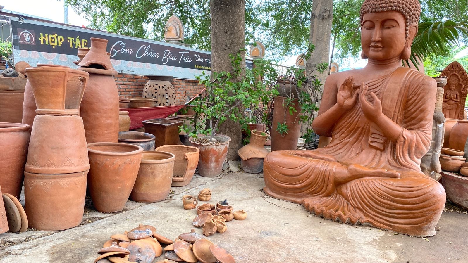 The yard of the Bau Truc pottery co-operative: unglazed red jars, water pots and a seated clay Buddha standing about in the shade