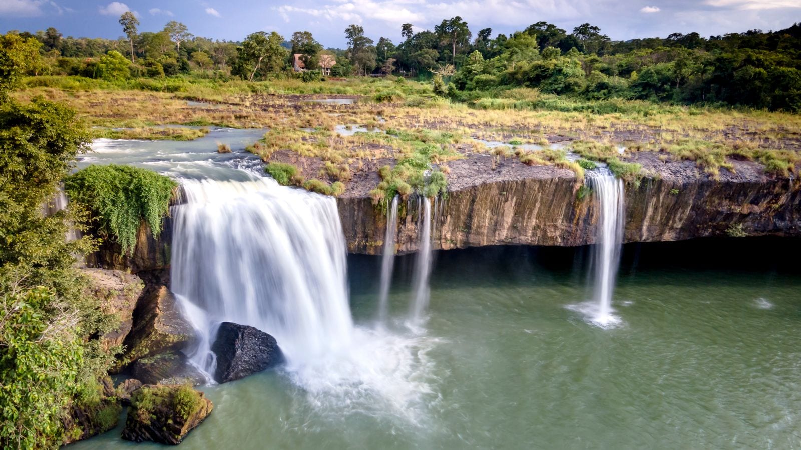 A waterfall dropping in two curtains over a flat basalt lip into a wide green pool, forest along the top of the cliff