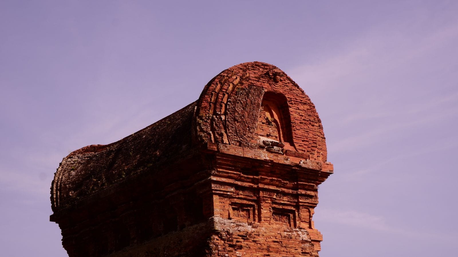 The top of a Cham brick tower against a violet sky, its curved roof carved with a niche and mouldings, moss growing along the ridge