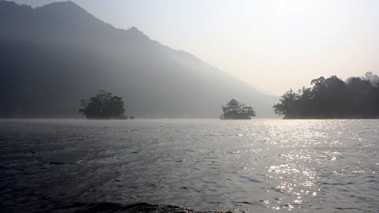 Mist lying on a lake at first light, two wooded islets standing out of the water and a forested ridge closing the far side