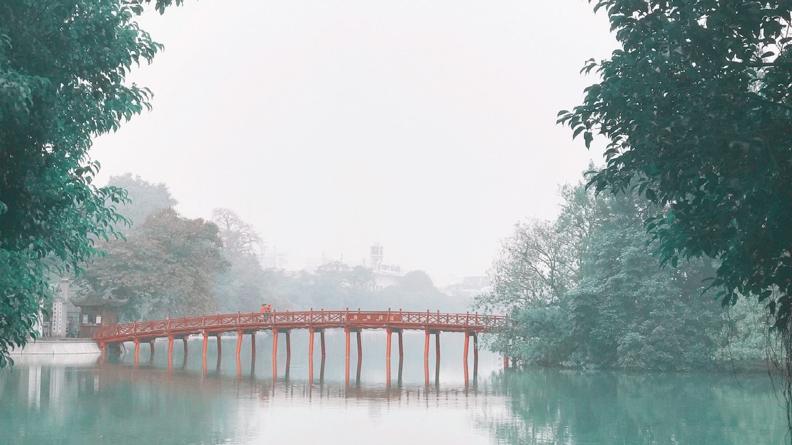 The red wooden bridge to Ngoc Son temple on Hoan Kiem lake, seen through trees in mist