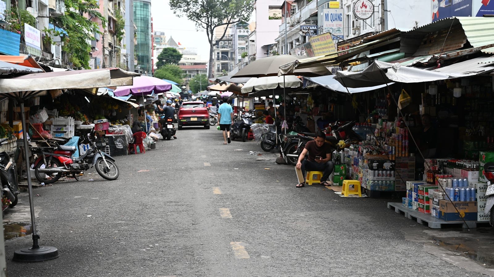 A Saigon market street lined with awnings, stalls and stacked beer crates