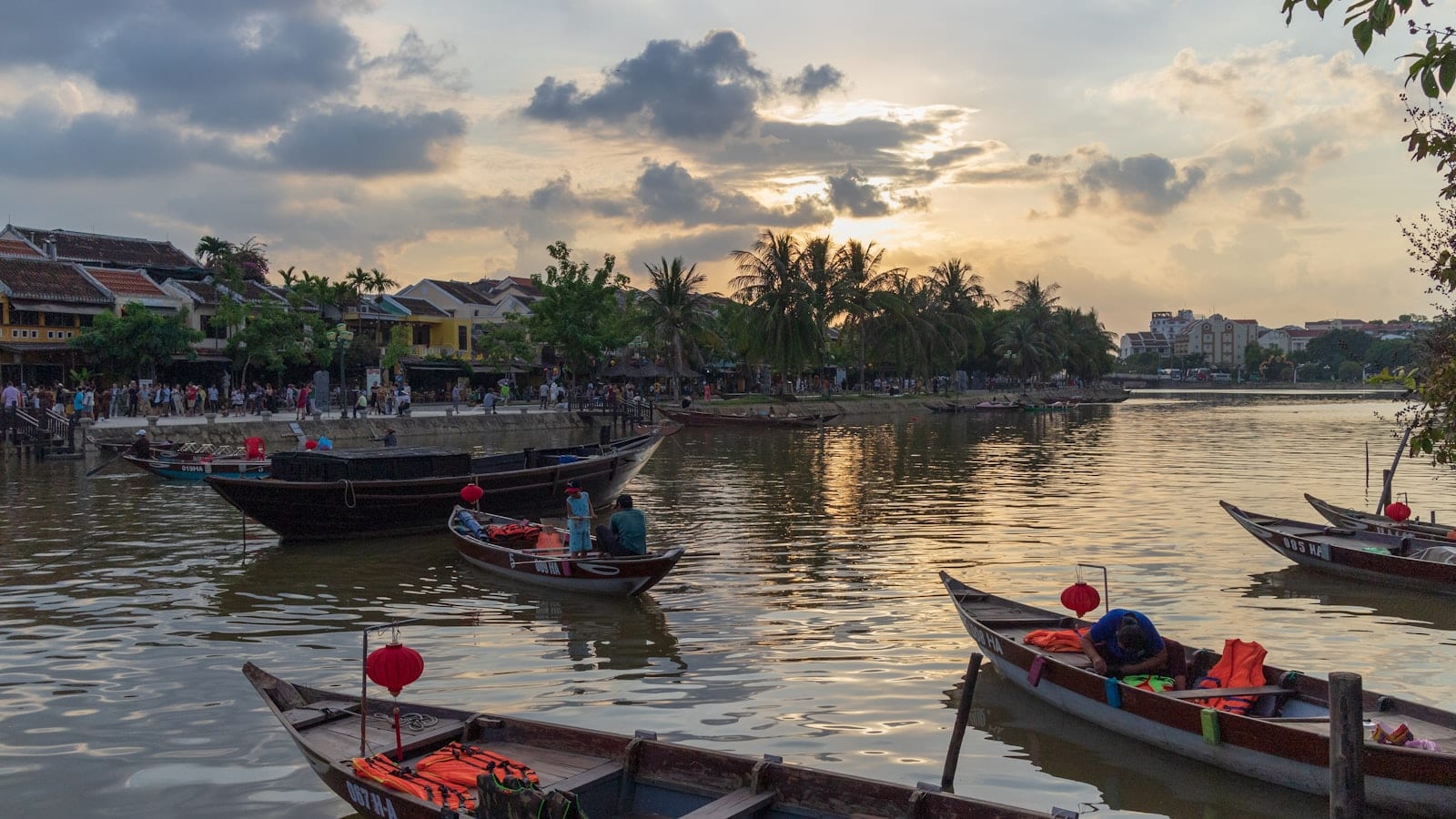 Wooden boats moored on the Thu Bon river at sunset, the old town's tiled roofs behind