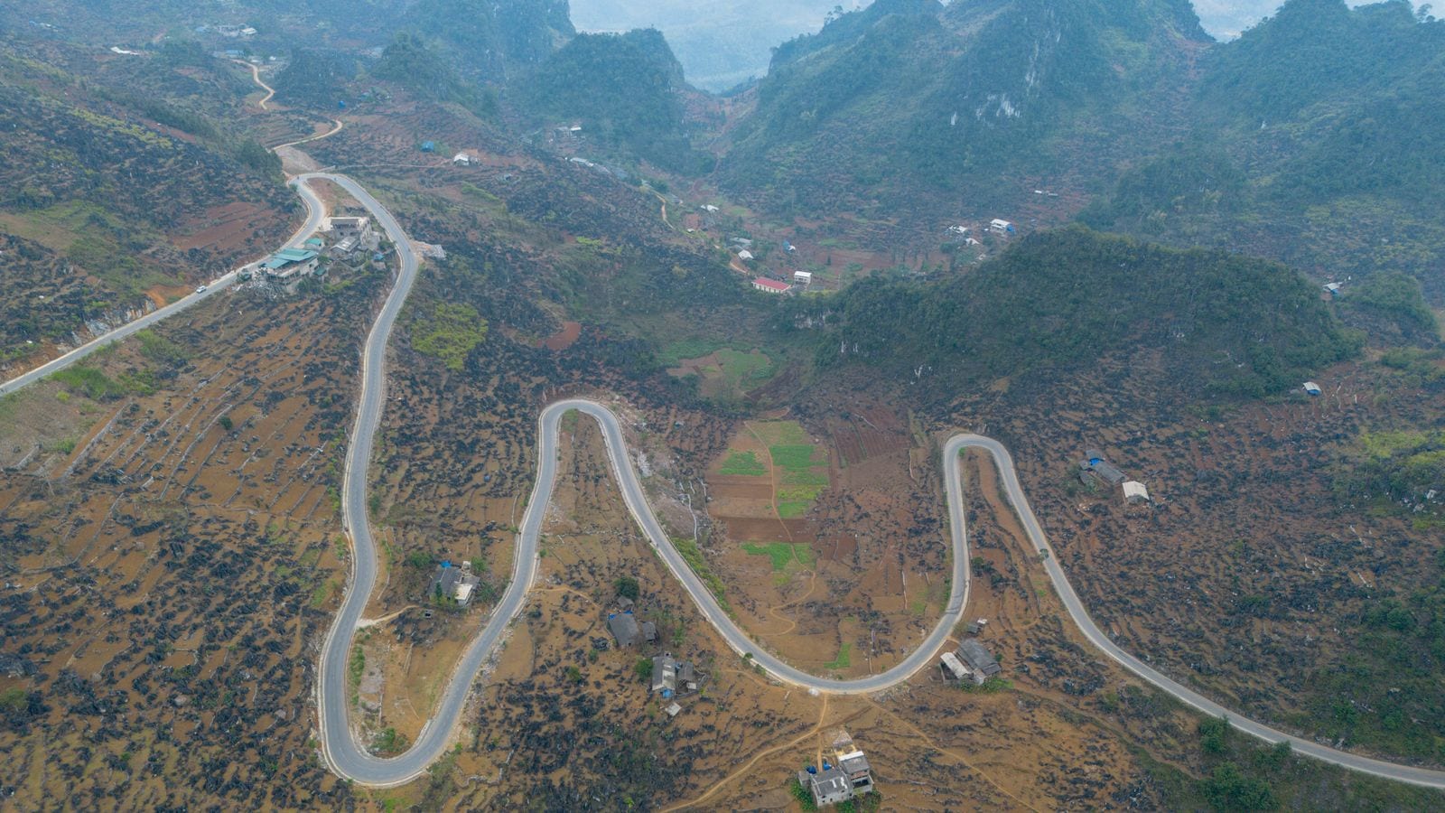 A road switchbacking three times across a plateau of black karst, maize plots and tin-roofed houses scattered between the bends