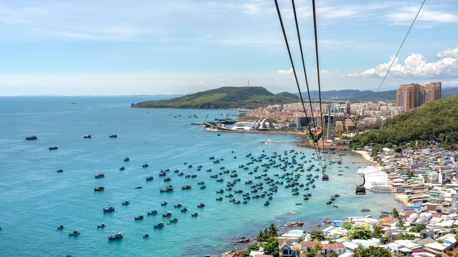 The cable car running out over a harbour packed with blue fishing boats, its cabins hanging from the span with the resort town and headlands beyond