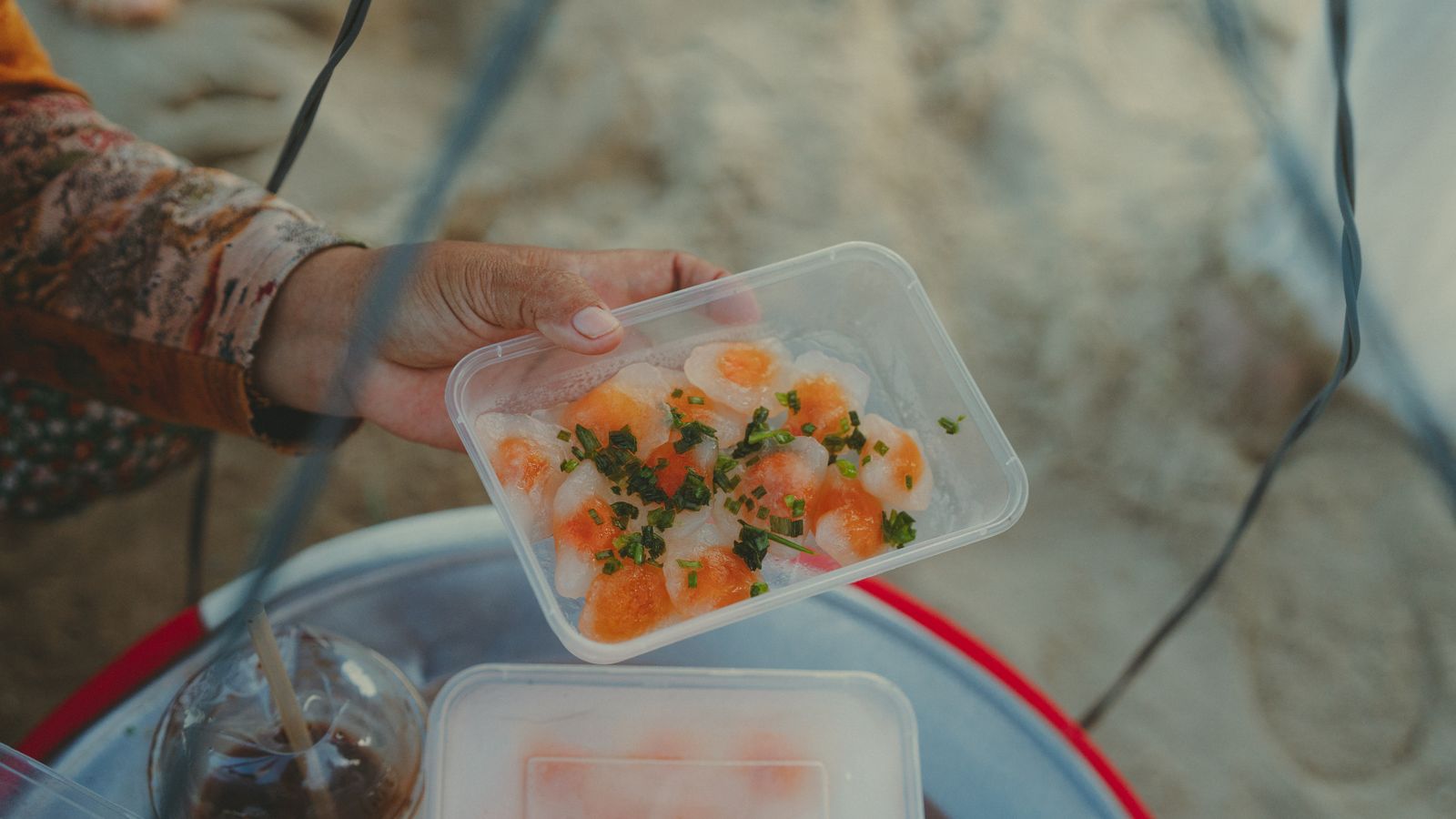 A plastic tray of banh bot loc held out by a vendor's hand: translucent dumplings showing orange prawn inside, topped with chopped spring onion
