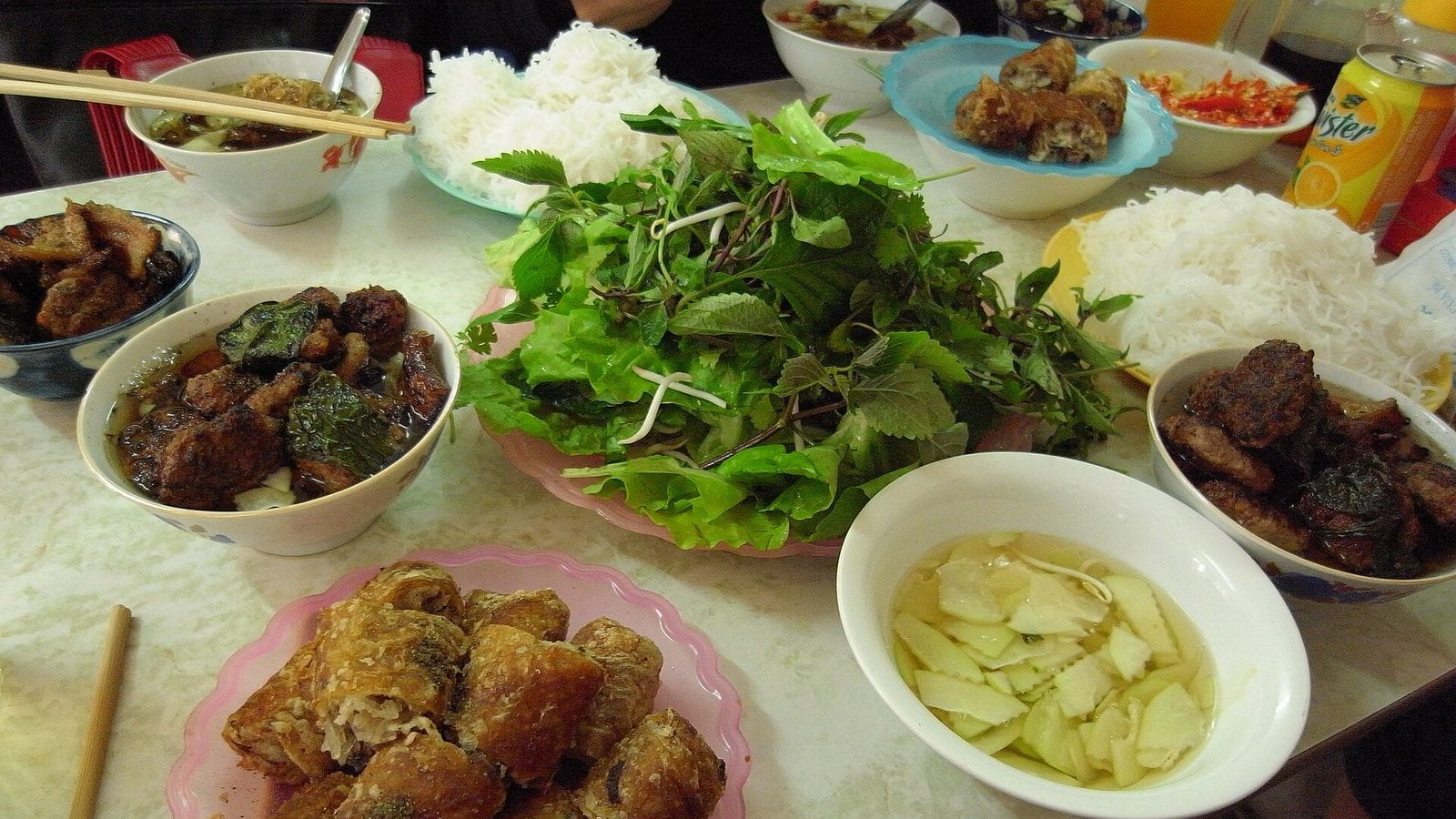 A bun cha table at Hang Manh: bowls of grilled pork in broth, plates of rice vermicelli, a heaped plate of herbs and lettuce, fried nem and pickled kohlrabi