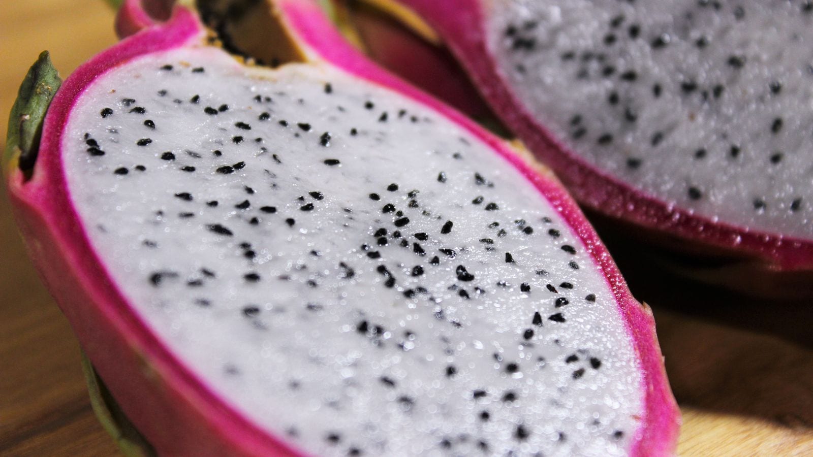 A dragon fruit cut in half showing white flesh and black seeds inside a bright pink skin