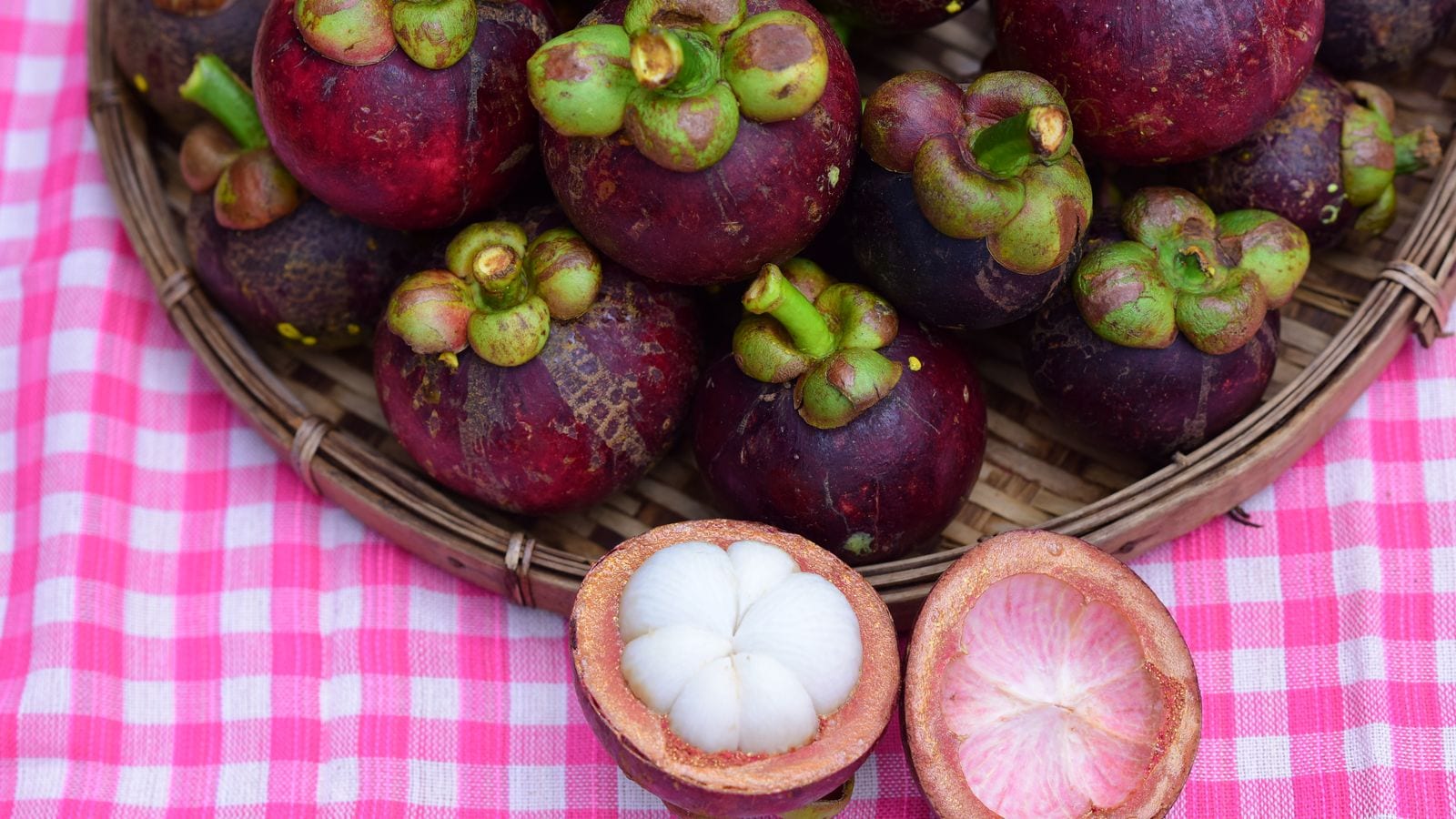 A basket of purple mangosteens with two cut open, showing the white segments inside the shell