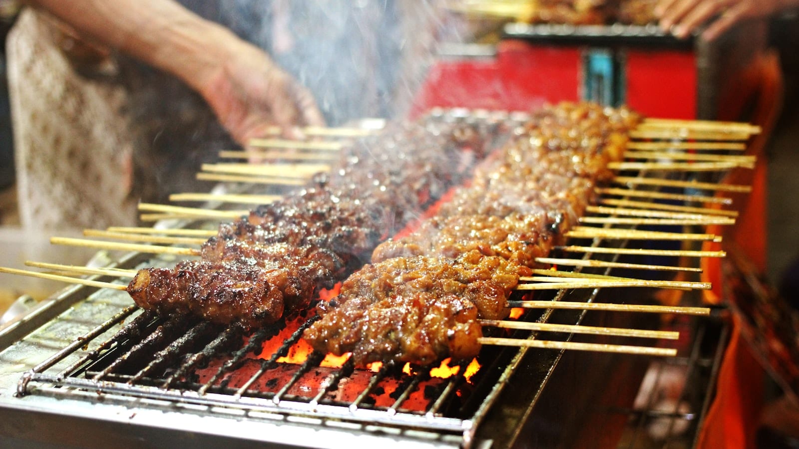 Skewers of marinated meat grilling over charcoal at a street stall