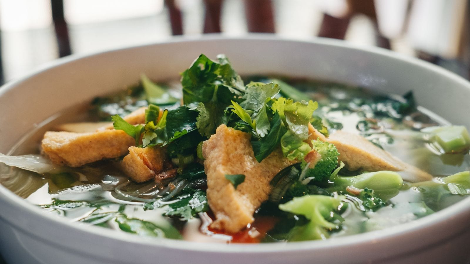 A vegetarian noodle bowl in clear broth with fried tofu, broccoli, greens and coriander