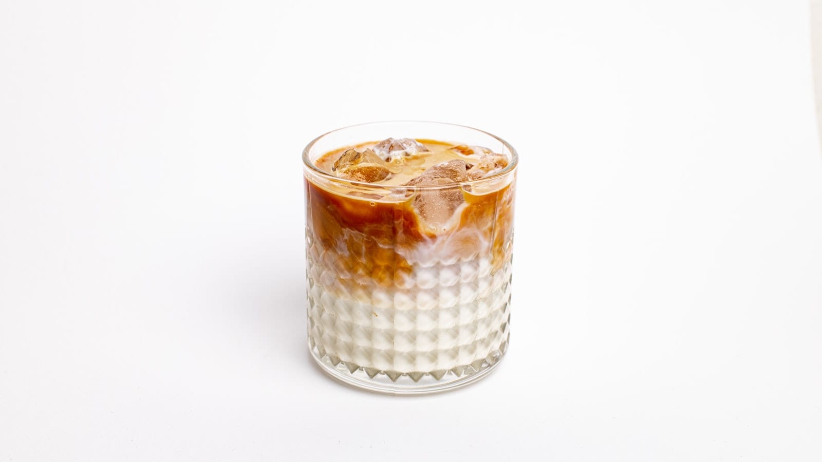 A short glass of iced coffee with a thick layer of condensed milk settled at the bottom
