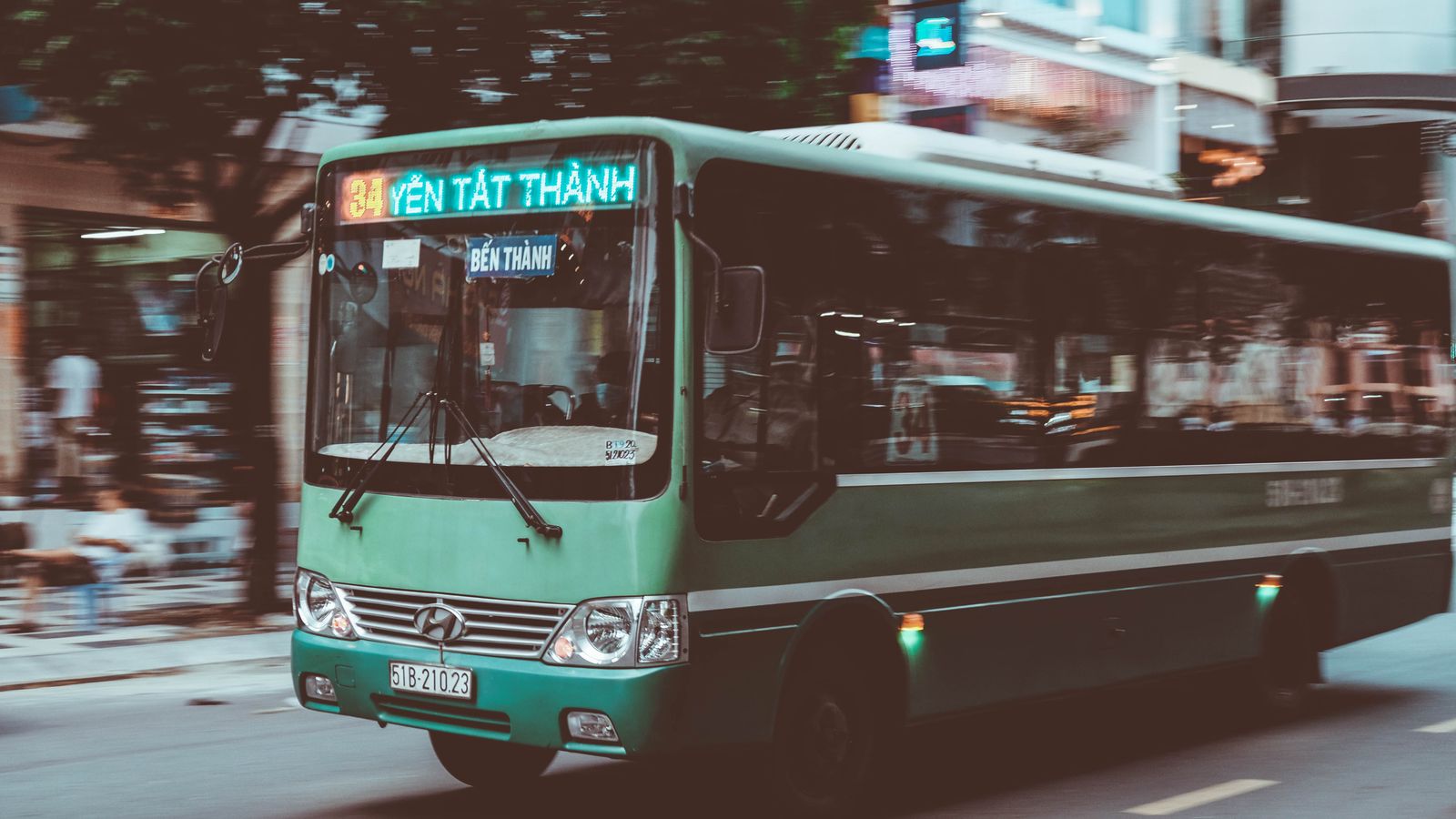 A green city bus running route 34 to Ben Thanh, destination board lit up above the windscreen, blurred street behind it