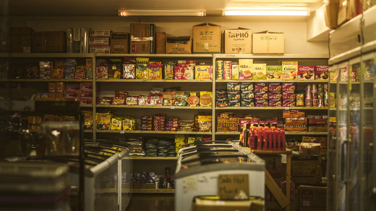 Shelves of Omachi and Vifon instant noodles, Hura cakes, Chin-su sauces and boxed Cafe Pho, with chest freezers down the middle of the shop