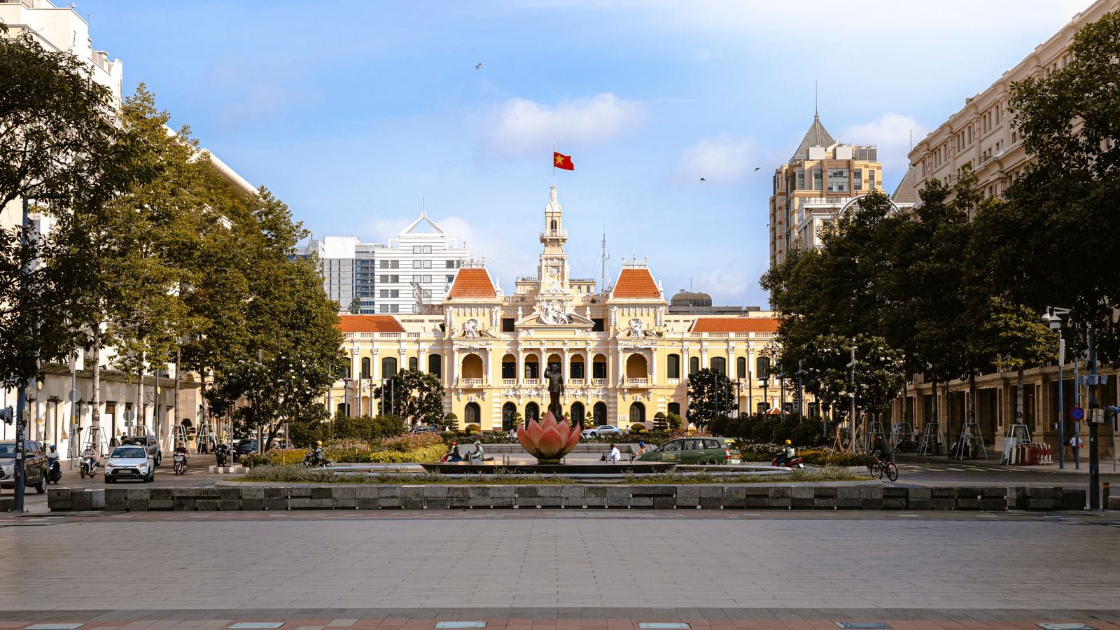 A colonial city hall in cream and ochre at the head of a wide pedestrian street, a flag on its tower and a lotus fountain on the paving in front