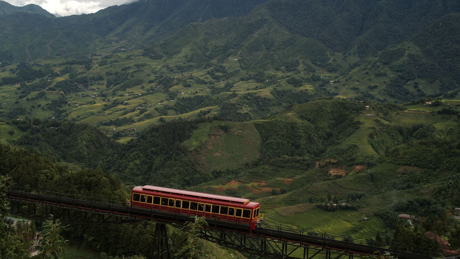 The red and yellow Muong Hoa funicular car climbing its viaduct above terraced valleys below Sapa