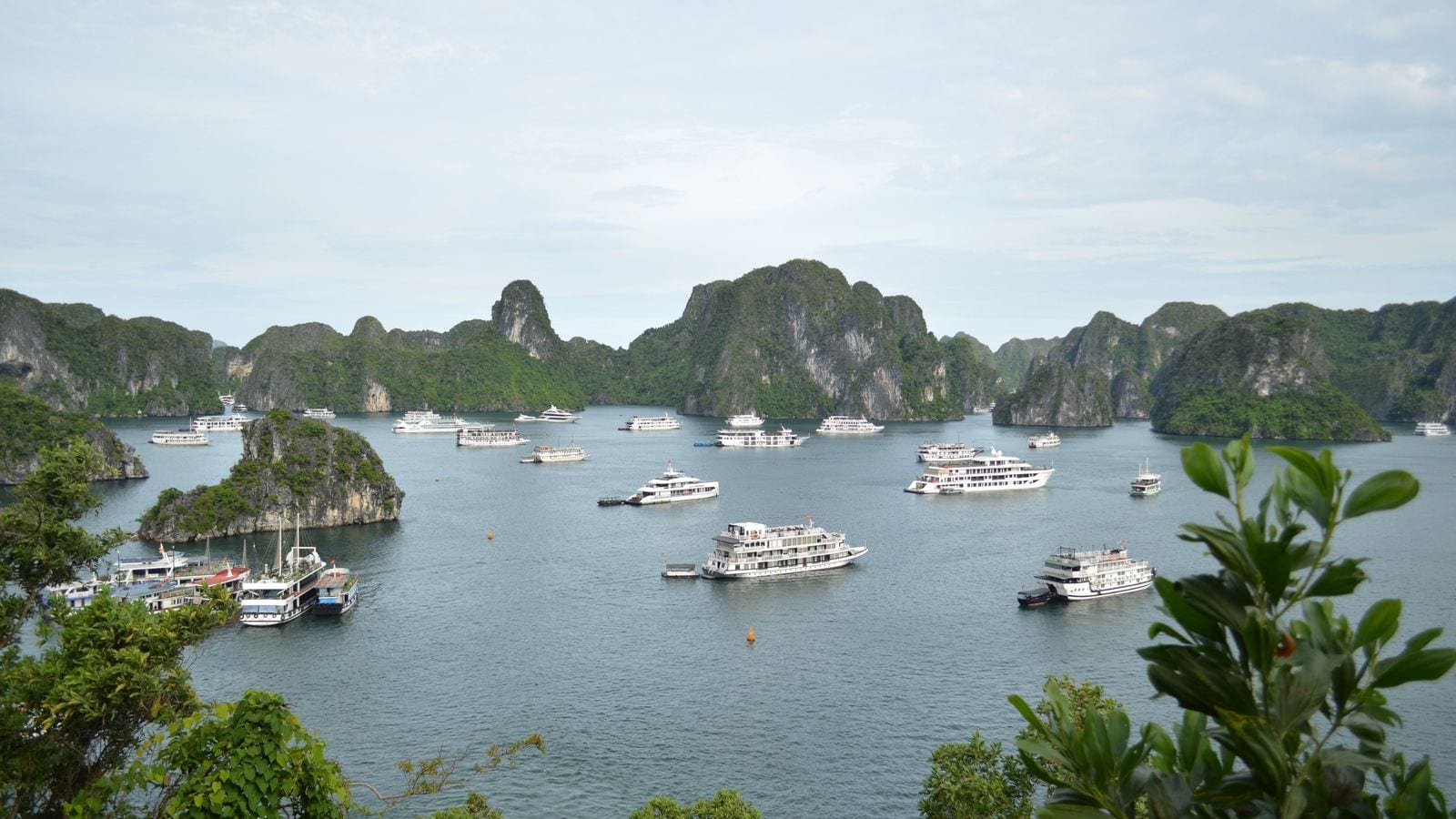 Limestone islands in Ha Long Bay with two dozen white cruise boats anchored between them