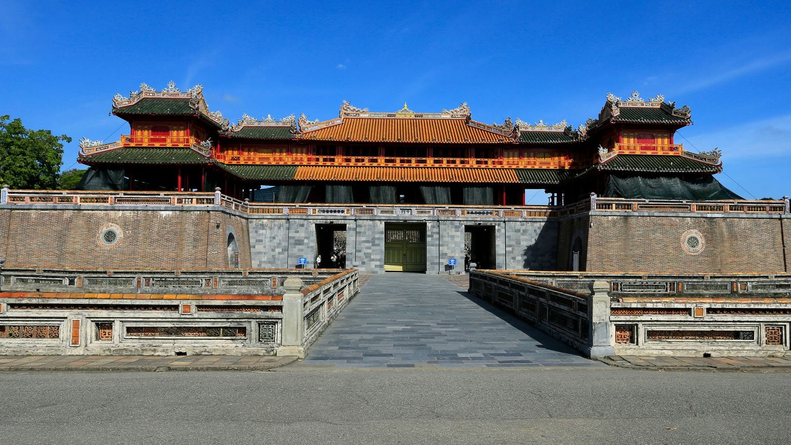 The Meridian Gate of the Hue citadel, its yellow-tiled pavilion above a brick rampart, an empty stone causeway leading in