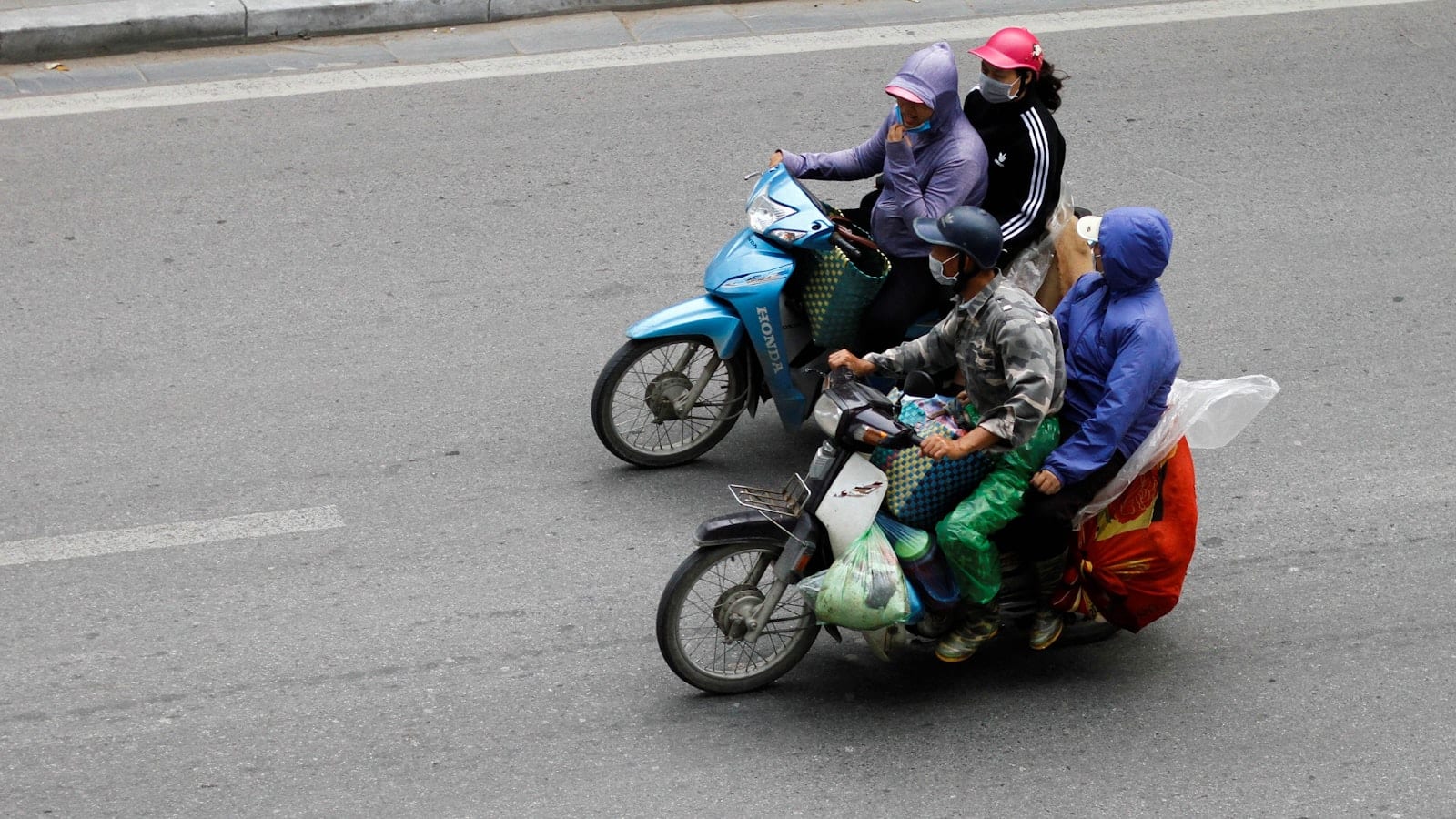 Two loaded motorbikes crossing a wide road, riders in helmets and rain jackets