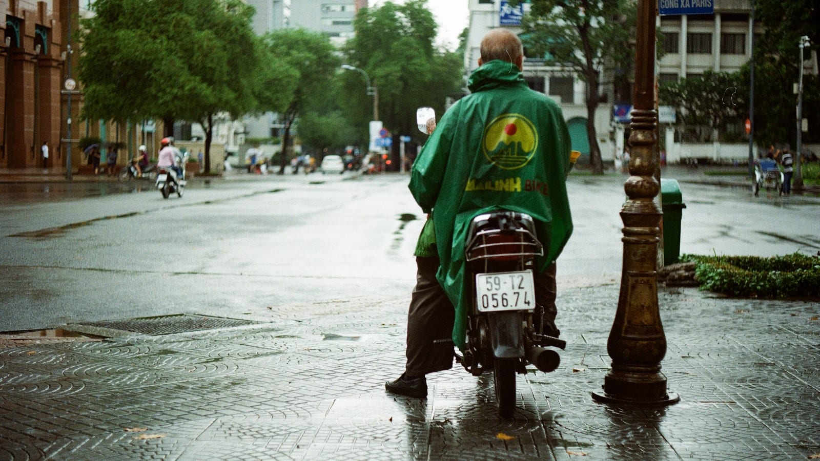A rider in a green plastic poncho waiting out the rain on a wet city street