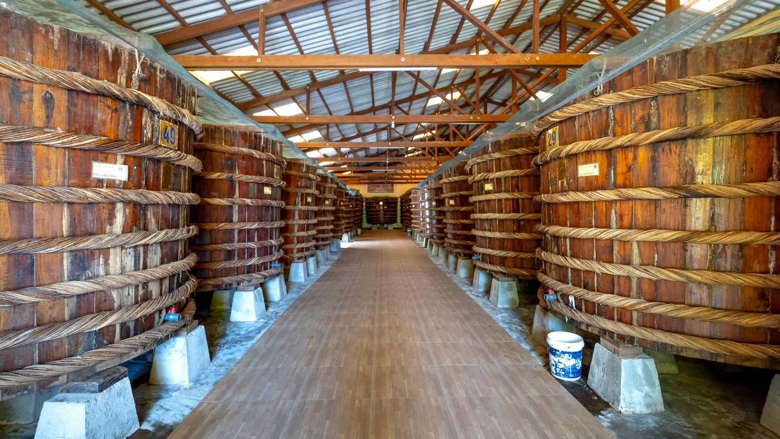 Rows of wooden fish sauce vats bound with rattan rope in a Phu Quoc factory, each numbered