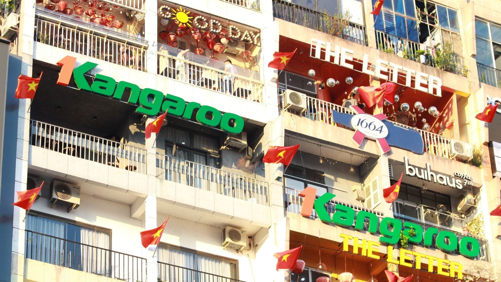 Stacked balconies of a Saigon apartment block carrying cafe and shop signs in English, Vietnamese flags hanging between them