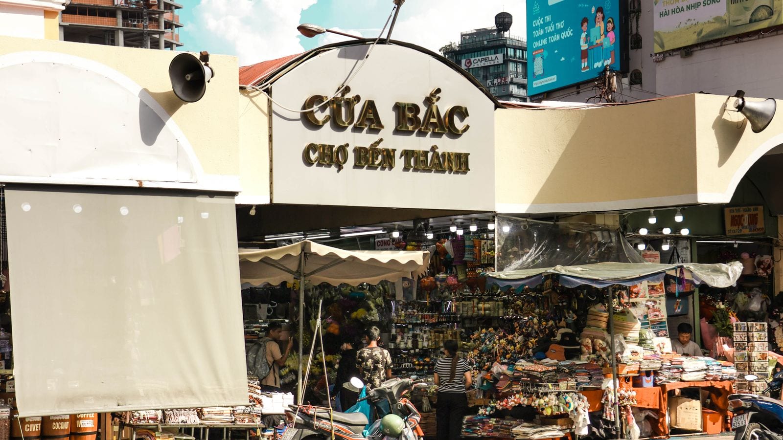 The north gate of Ben Thanh market in Saigon, gold letters reading Cua Bac Cho Ben Thanh above stalls of bags and souvenirs
