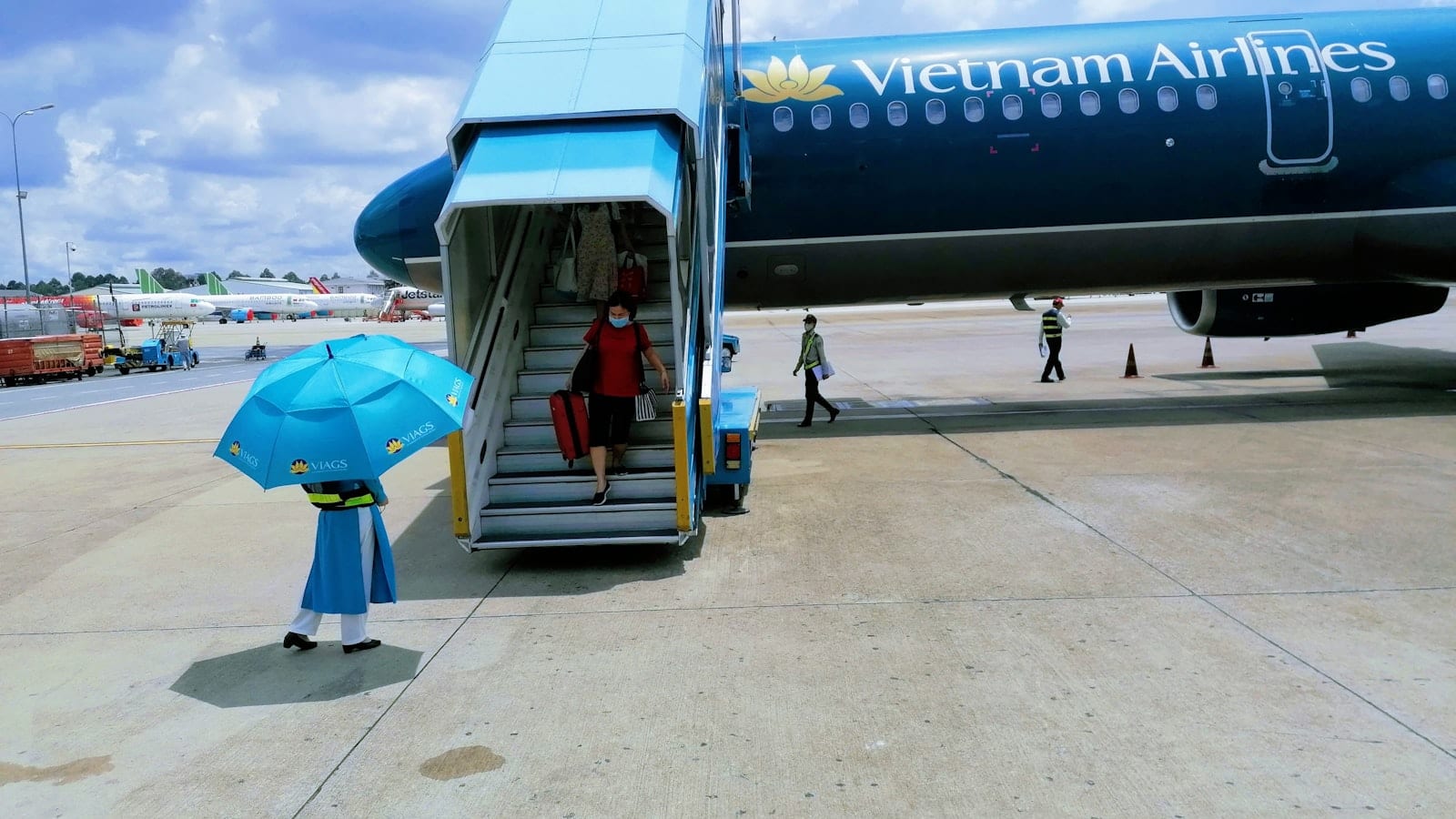 Passengers walking down aircraft steps onto the apron at a Vietnamese airport