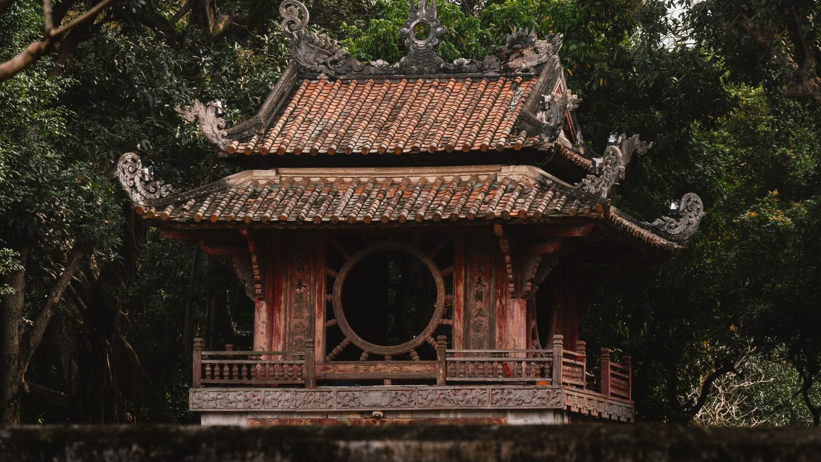 The Khue Van Cac pavilion at the Temple of Literature, a round window in each side of the upper storey, tiled roofs curling up at the corners above red timber posts