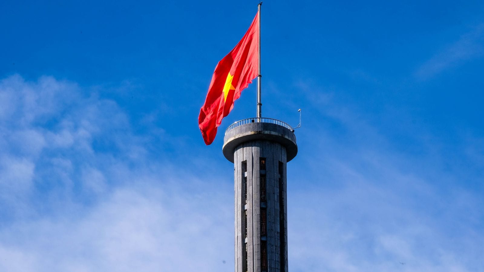 The Lung Cu flag tower against a blue sky, an oversized national flag streaming from the pole above its octagonal viewing platform