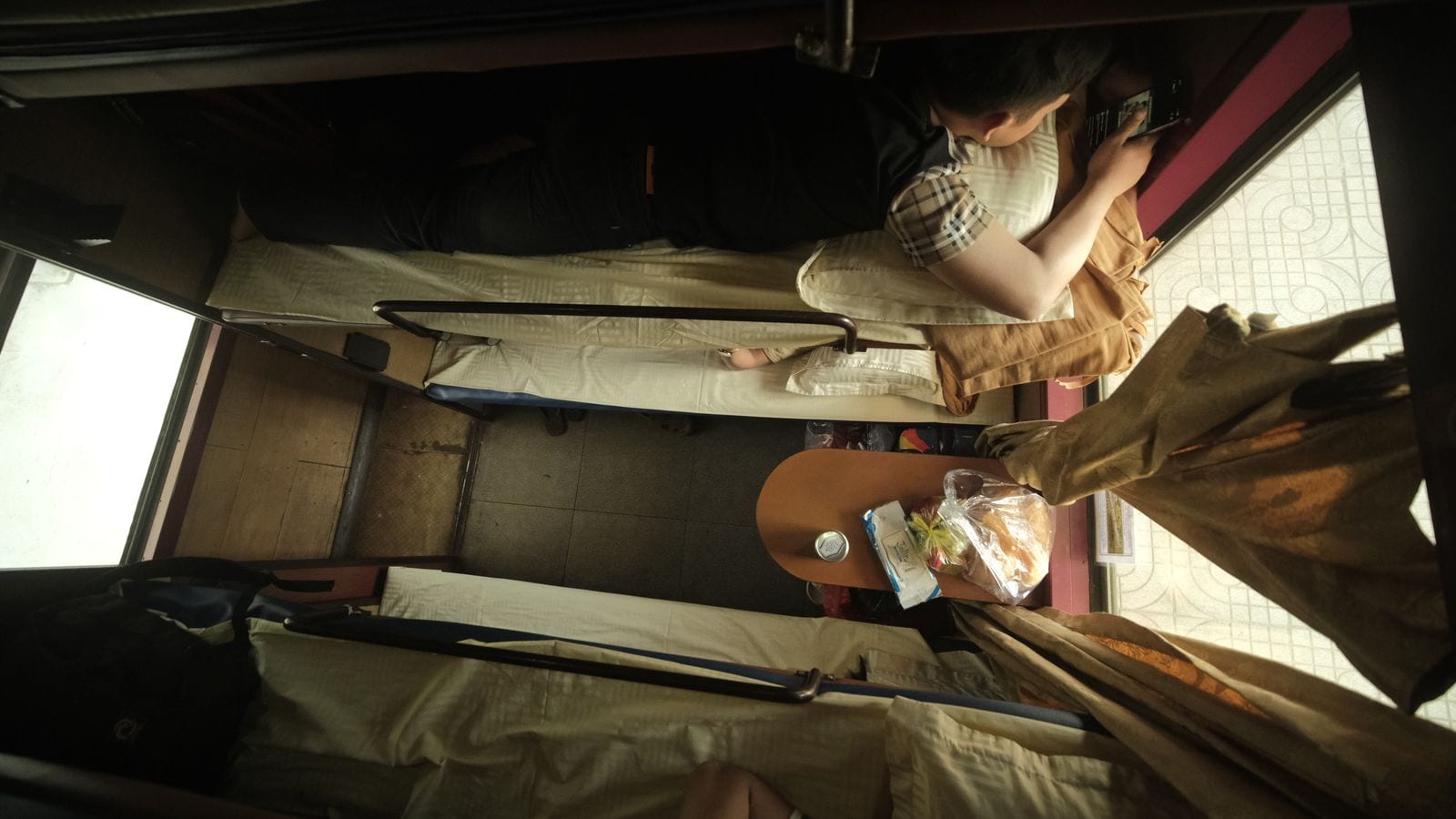A four-berth soft sleeper compartment on a Vietnamese train, two bunks made up on each side with a small table between them holding bread and a drink