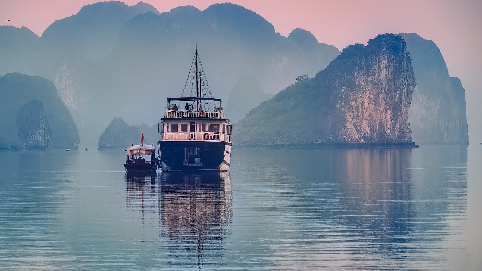A cruise boat anchored among the limestone islands of Ha Long Bay at dawn
