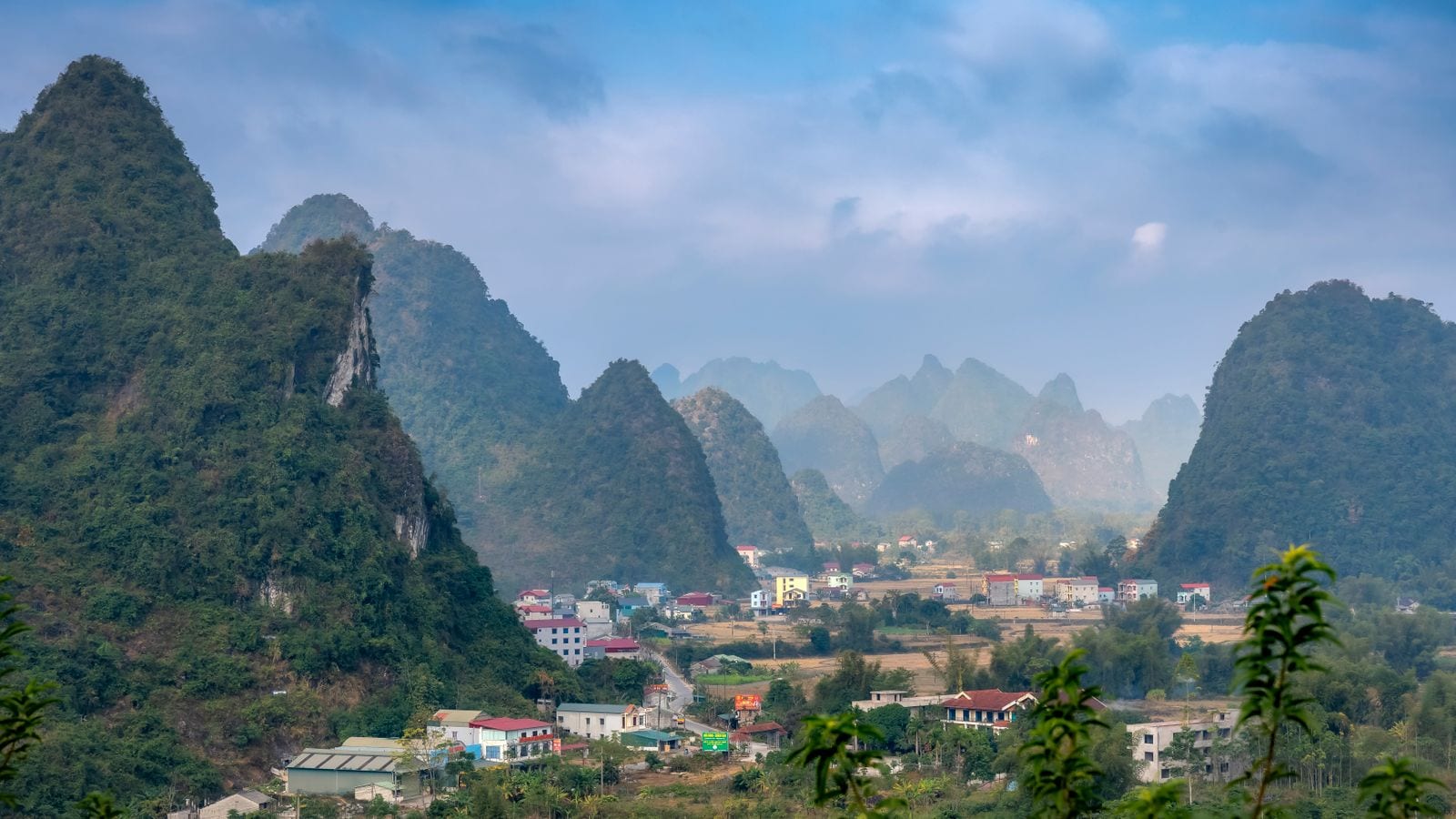 A small town spread along a road between limestone towers, painted houses and cut fields in the valley floor and ridges fading back into haze