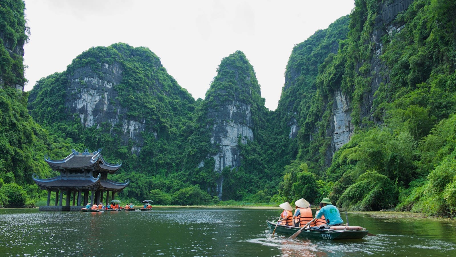 Rowing boats on a green river between limestone cliffs, a wooden pavilion on the bank