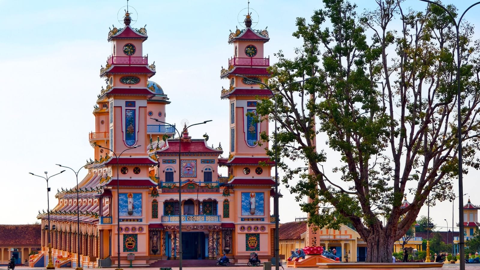 A Cao Dai temple in pink and pale yellow, twin bell towers at the front and the divine eye painted in a blue panel above the entrance