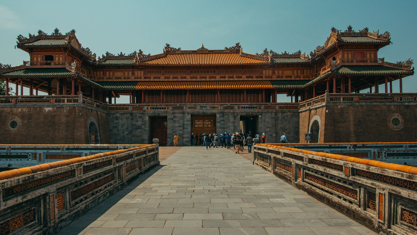 The Ngo Mon gate of the Hue citadel seen straight on across the bridge, yellow tiled pavilion on top of the stone gatehouse, with a group walking through the central arch