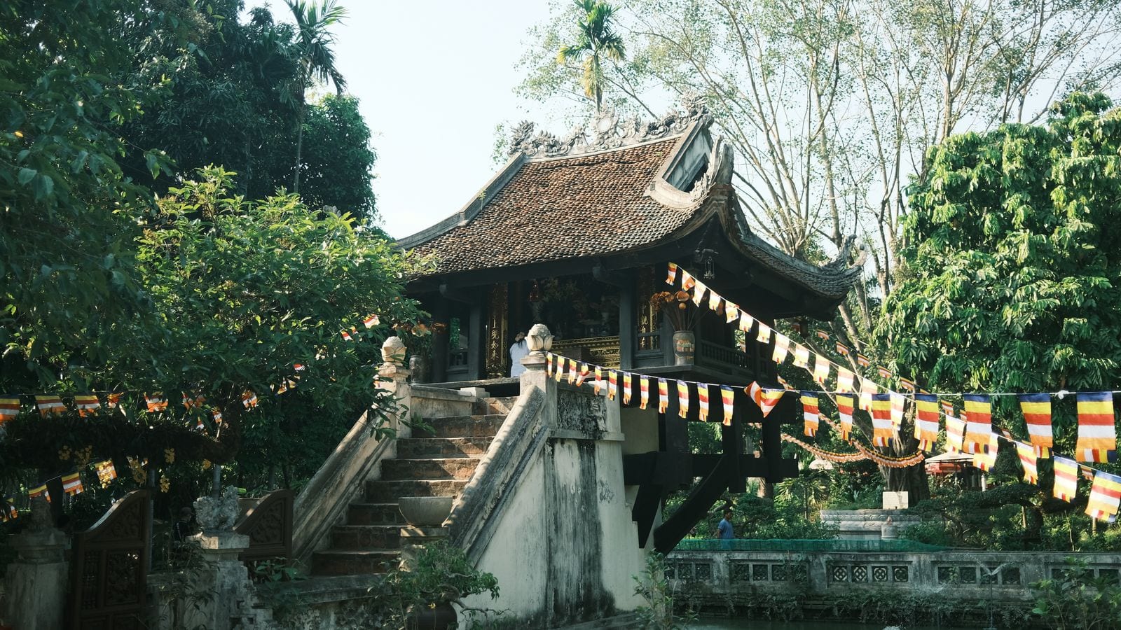 The One Pillar Pagoda on its single stone column above the pond, tiled roof curling at the corners, with strings of Buddhist flags hung across the front