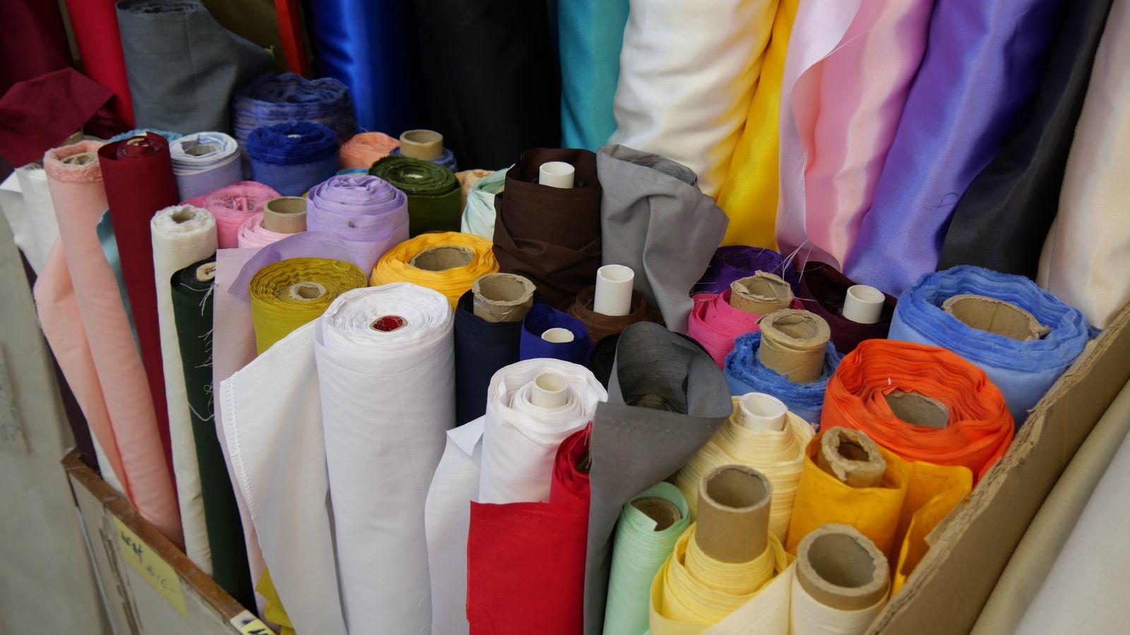Bolts of cloth stood on end in a wooden crate — silk, cotton and lining in every colour, some rolled on tubes and some folded over the rim