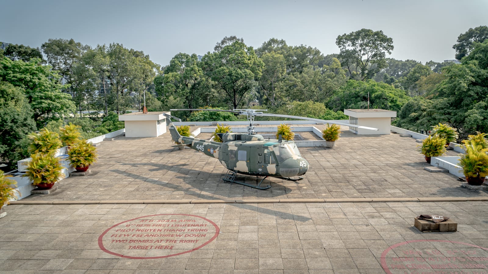 A camouflaged UH-1 helicopter parked on the roof terrace of the Independence Palace, with a red circle painted on the tiles marking where a bomb was dropped in April 1975