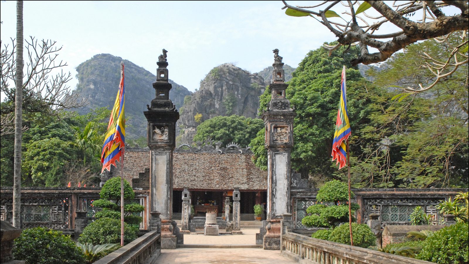 The stone gate pillars and tiled roof of the temple to King Dinh Tien Hoang at Hoa Lu, festival flags either side and limestone peaks behind